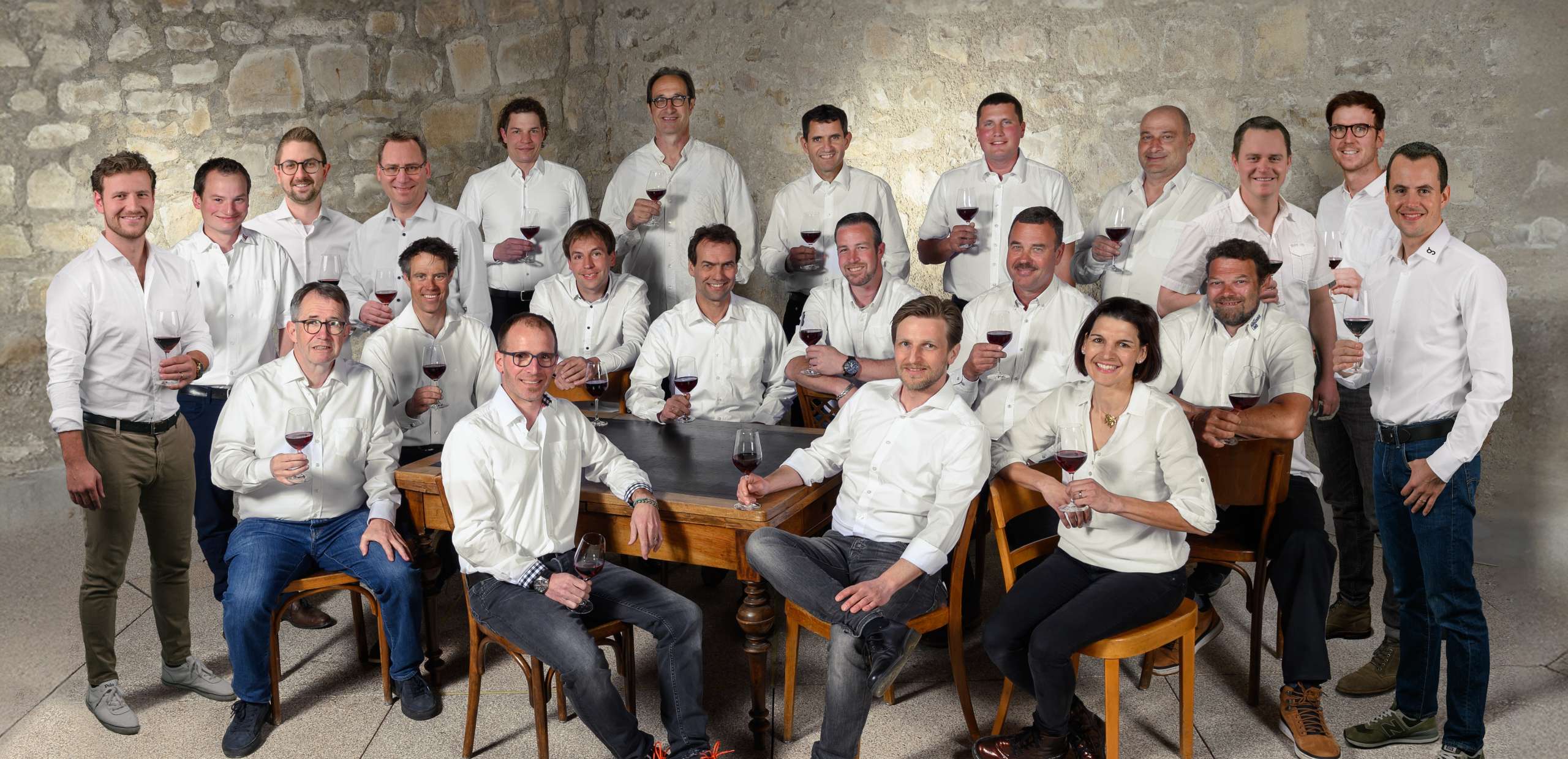 Gruppenbild Winzer. Aller tragen ein weisses Hemd und haben ein Rotweinglas in der Hand.